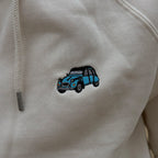Primo piano del ricamo Citroën 2CV azzurro cielo sul tessuto felpato ecru, vicino al cordino del cappuccio