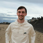 Ecru Overcut hooded sweatshirt with Porsche 911 embroidery, worn on a beach